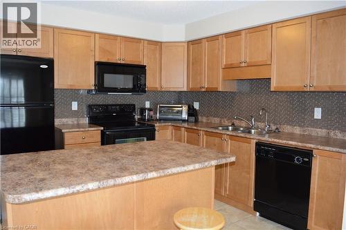 Kitchen featuring light wood-finish cabinetry, black appliances, a tile backsplash, and an island with a laminate countertop - 507 Beaumont Crescent, Kitchener, ON 