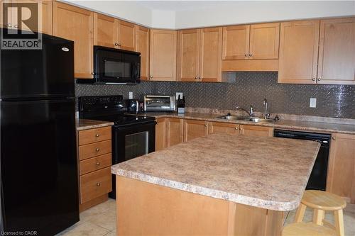 Maple wood-finish cabinetry, black appliance suite, textured metal backsplash, L-shaped counter space, and a center island with a laminate countertop - 507 Beaumont Crescent, Kitchener, ON 
