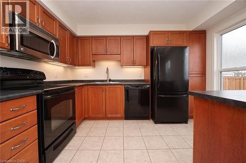 Wood-finish cabinetry with silver-tone hardware, stainless steel microwave, black range, integrated black dishwasher, and black refrigerator - 250 Parkvale Drive, Kitchener, ON 