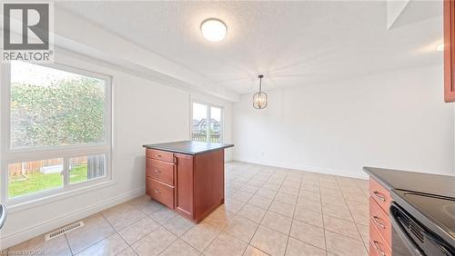 Tile flooring, white walls, kitchen island with dark countertop, pendant light fixture, and sliding glass door - 250 Parkvale Drive, Kitchener, ON 