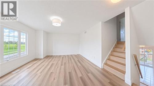 Light wood-finish flooring, white walls, large window with grid pattern, neutral ceiling light fixture, and a wood staircase with railing - 250 Parkvale Drive, Kitchener, ON 