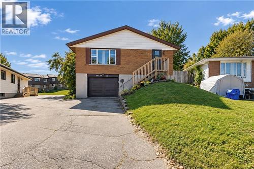 Brick exterior with a brown garage door, front entry stairs, and a sloped lawn - 135 Cedarhill Crescent, Kitchener, ON 
