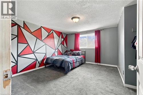 Carpeted room featuring a geometric accent wall, painted walls, a window with natural light, and a ceiling-mounted light fixture - 135 Cedarhill Crescent, Kitchener, ON 