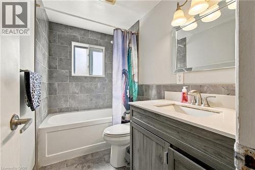 Bathroom featuring a vanity with a white countertop, a mirror with decorative trim, and a bathtub with gray tiled walls - 135 Cedarhill Crescent, Kitchener, ON 