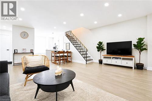 Recessed lighting, light wood-finish flooring, open-tread staircase with metal railing, dining area with built-in cabinetry, and white painted walls - 136 Jansen Avenue, Kitchener, ON 