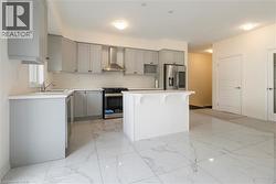 Kitchen featuring stainless steel appliances, gray cabinets, wall chimney exhaust hood, a center island, and light marble finish flooring - 