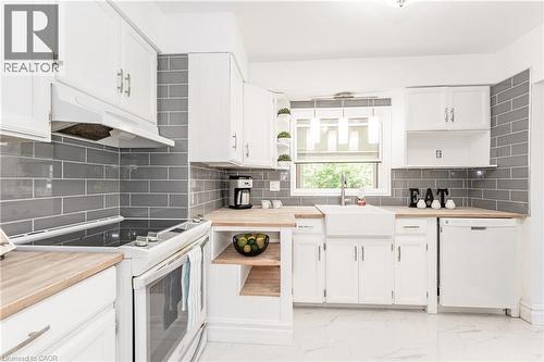 White shaker-style cabinetry with chrome hardware, wood-finish countertops, grey subway tile backsplash, and a white farmhouse sink - 388 Appleby Line, Burlington, ON 