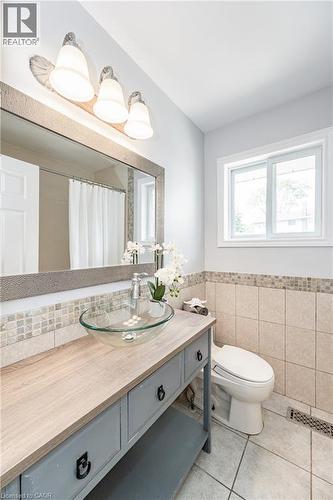 Glass vessel sink, wood-finish vanity top, tile wainscoting, and a window providing natural light - 388 Appleby Line, Burlington, ON 