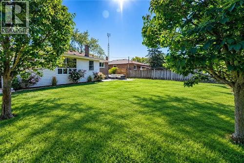 Expansive green lawn with mature trees, a white-sided residence featuring large windows, and a privacy fence - 388 Appleby Line, Burlington, ON 