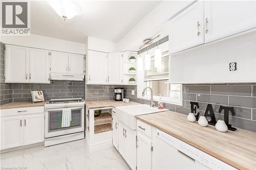 White cabinetry with brushed nickel hardware, light wood-finish countertops, gray subway tile backsplash, white farmhouse sink, and white appliances - 388 Appleby Line, Burlington, ON 