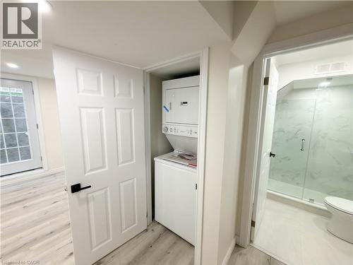 Integrated stacked washer and dryer within a dedicated closet, three-panel interior door with black hardware, wood-finish flooring, and a walk-in shower with glass enclosure and tiled walls - 304 Westpark Crescent, Waterloo, ON 