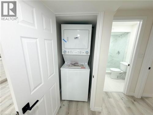Compact laundry area featuring a stacked washer and dryer, adjacent to a bathroom with a glass-enclosed shower, white toilet, and light-toned flooring - 304 Westpark Crescent, Waterloo, ON 