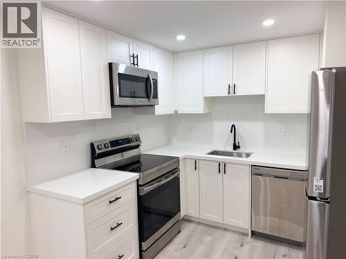 Modern kitchen featuring white shaker cabinetry with black hardware, stainless steel appliances including a built-in microwave and electric range, white quartz countertops, an undermount sink with mat - 304 Westpark Crescent, Waterloo, ON 