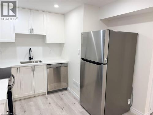 White shaker cabinetry, stainless steel appliances, light wood-finish flooring, undermount sink, and black matte faucet - 304 Westpark Crescent, Waterloo, ON 
