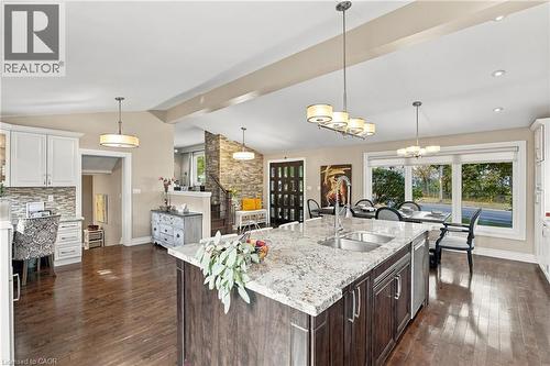 Wood-finish flooring, central island with granite countertop and double sink, white cabinetry with tile backsplash, multiple pendant light fixtures, and expansive windows - 617 Scenic Drive, Hamilton, ON 