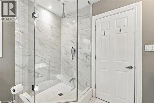 Glass-enclosed shower with a rainfall showerhead, integrated shelving, and white marble-patterned tile - 617 Scenic Drive, Hamilton, ON 