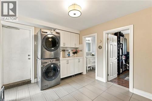 Stacked stainless steel laundry appliances, white cabinetry with silver hardware, recessed ceiling light fixture, tile flooring, and a paneled interior door - 617 Scenic Drive, Hamilton, ON 