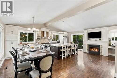 Vaulted ceiling with exposed beams, wood-finish flooring, white cabinetry, integrated fireplace, and a large kitchen island with seating - 617 Scenic Drive, Hamilton, ON 