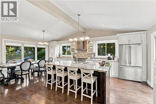 Vaulted ceiling kitchen featuring a large central island with seating, stainless steel appliances, white cabinetry, and wood-finish flooring - 617 Scenic Drive, Hamilton, ON 