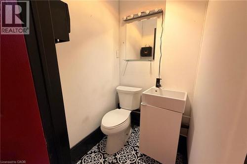 White pedestal sink with a matte black faucet, wall-mounted mirror with integrated lighting, and patterned floor tiling - 319 King Street E, Hamilton, ON 