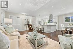 Open-concept living space featuring hardwood flooring, recessed ceiling lighting, and a glass-top coffee table with shelving - 