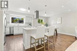 Open-concept kitchen with white cabinetry, stainless steel appliances, a center island with seating, and wood-finish flooring - 