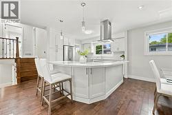 Chef's kitchen showcasing white cabinetry, stainless steel appliances including a gas range with overhead hood, waterfall-edge quartz island with seating for multiple, pendant lighting, and wood-finis - 