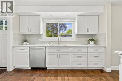White shaker cabinetry, stainless steel dishwasher, white countertops, mosaic tile backsplash, and wood-finish flooring - 