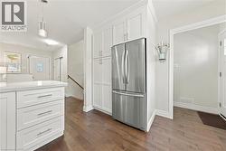 Contemporary kitchen showcasing crisp white cabinetry with ample storage, stainless steel French-door refrigerator, wood-finish flooring throughout, and a bright, open layout with recessed lighting an - 