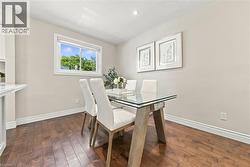 Bright dining space featuring a glass-top table with natural wood base, upholstered dining chairs, and hardwood flooring throughout - 