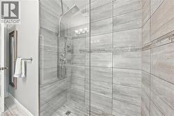 Spa-inspired shower enclosure featuring large-format porcelain tile walls with horizontal striping, frameless glass enclosure, dual showerheads with rainfall and handheld options, and brushed nickel f - 