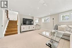 Recessed lighting, light-toned carpeting, wood staircase, two windows with plantation shutters, and a ceiling fan - 
