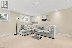 Finished basement recreation room featuring a neutral color palette, recessed ceiling lighting, picture windows with plantation shutters, neutral carpet flooring, and crown molding throughout - 