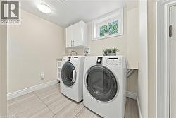 Modern laundry room featuring side-by-side front-load washers and dryers with white cabinetry, wood-finish flooring, recessed ceiling lighting, and a high window for natural light - 
