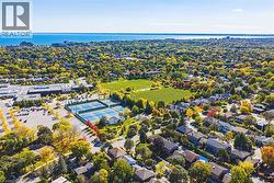 Aerial perspective featuring a body of water, extensive green spaces, multiple tennis courts, and residential rooftops among mature trees - 