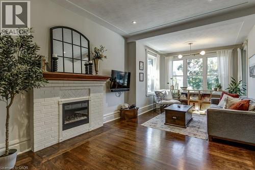 Hardwood flooring, white brick fireplace with mantel, recessed lighting, large windows, and a built-in ceiling light fixture - 43 Rosslyn Avenue S, Hamilton, ON 
