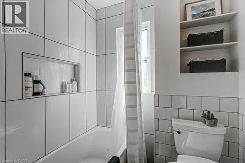Bathtub with a tiled surround featuring a recessed niche, vertical and horizontal tile patterns, and a window - 43 Rosslyn Avenue S, Hamilton, ON 