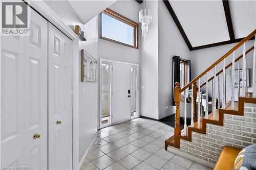 Vaulted ceiling with exposed beams, wood-finish staircase with white balusters, brick-finish staircase wall, tile flooring, and a contemporary chandelier - 19 Hyslop Drive, Caledonia, ON 
