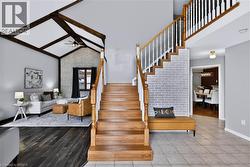 Wood-finish staircase with white balusters, vaulted ceiling with exposed beams, brick accent wall, and dark wood-finish flooring - 