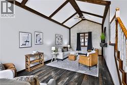 Vaulted ceiling with exposed beams, wood-finish flooring, white painted brick accent wall, ceiling fan, and staircase with wood railing - 