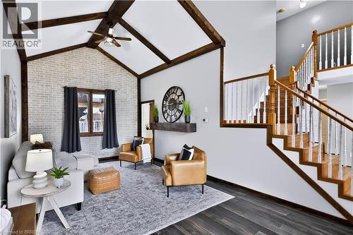 Vaulted ceiling with exposed wood beams, accent brick wall, wood-finish flooring, natural wood staircase with white balusters, and a recessed wall niche - 19 Hyslop Drive, Caledonia, ON 