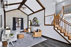 Vaulted ceiling with exposed wood beams, accent brick wall, wood-finish flooring, natural wood staircase with white balusters, and a recessed wall niche - 