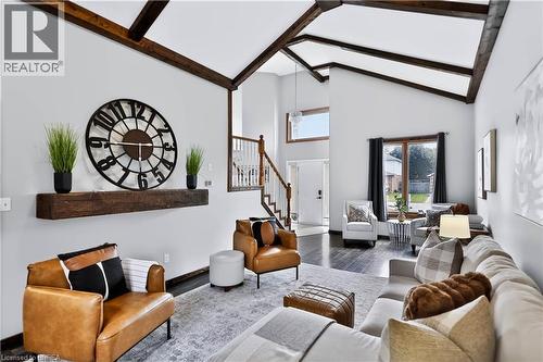 Vaulted ceilings with exposed wood beams, dark wood-finish flooring, staircase with wood handrail and white spindles, transom window, and a large picture window - 19 Hyslop Drive, Caledonia, ON 