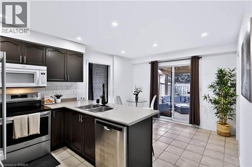 Kitchen featuring dark wood cabinetry, stainless steel appliances, a subway tile backsplash, and light-toned countertops - 19 Hyslop Drive, Caledonia, ON 