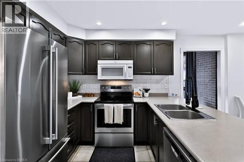 U-shaped kitchen featuring dark wood cabinetry, stainless steel appliances, a subway tile backsplash, light-toned countertops, and recessed lighting - 19 Hyslop Drive, Caledonia, ON 