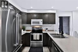 U-shaped kitchen featuring dark wood cabinetry, stainless steel appliances, a subway tile backsplash, light-toned countertops, and recessed lighting - 