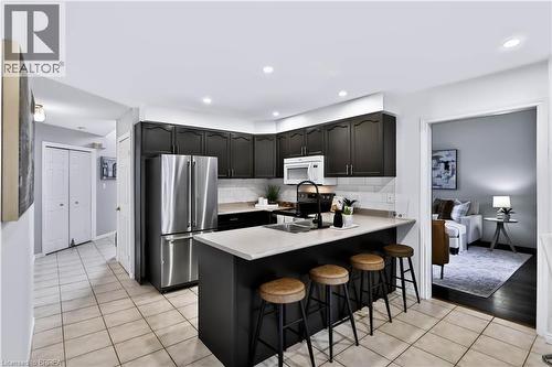 Kitchen featuring dark cabinetry, stainless steel appliances, a white subway tile backsplash, and a light-toned countertop island - 19 Hyslop Drive, Caledonia, ON 