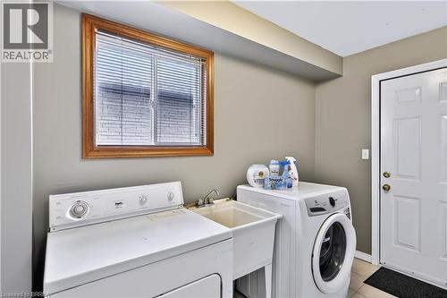 Dedicated laundry area featuring a utility sink, a multi-pane window with wood-finish trim, and a panel door with brass-finish hardware - 19 Hyslop Drive, Caledonia, ON 