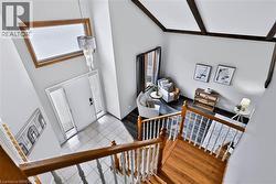 Vaulted ceiling with exposed wood beams, wood-finish flooring, white tiled entryway, natural wood staircase, and a contemporary chandelier - 