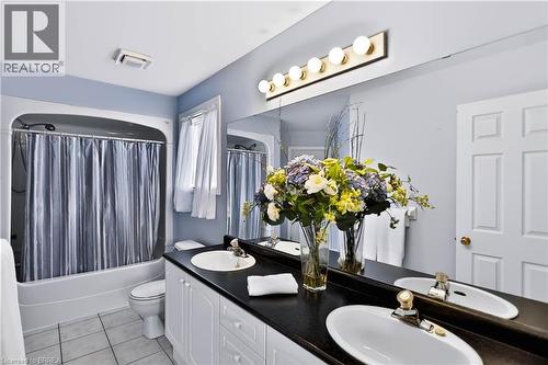 Double vanity with undermount sinks, black countertop, white cabinetry, and large wall-mounted mirror - 19 Hyslop Drive, Caledonia, ON 